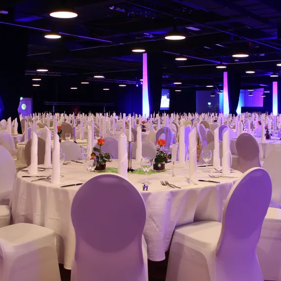 Festlich gedeckter Bankettsaal mit runden Tischen und lila Beleuchtung.