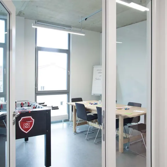 Besprechungsraum mit Tischkicker, Stühlen und großem Fenster.
