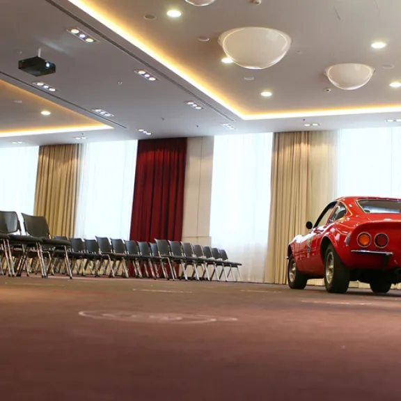Roter Oldtimer steht in einem modernen, leeren Konferenzraum mit Stuhlreihen.