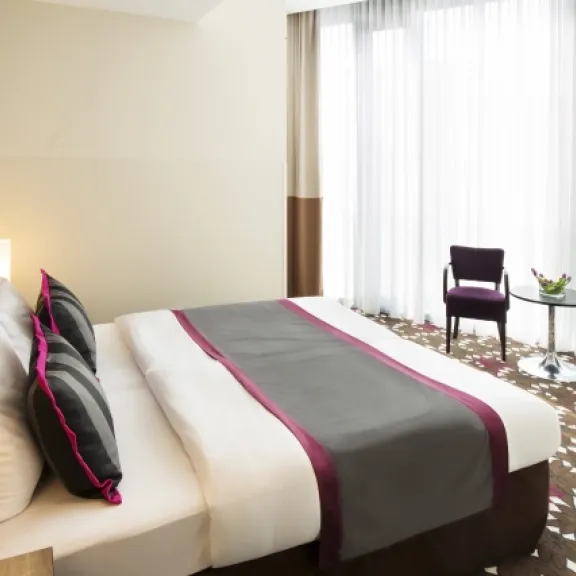 Modernes Hotelzimmer mit Doppelbett, zwei Stühlen und bodentiefen Fenstern.