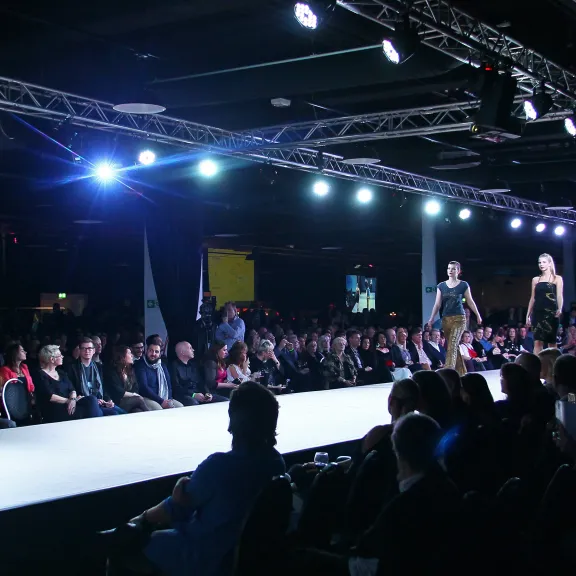 Modenschau mit Publikum, Laufsteg und Models unter hellen Scheinwerfern.