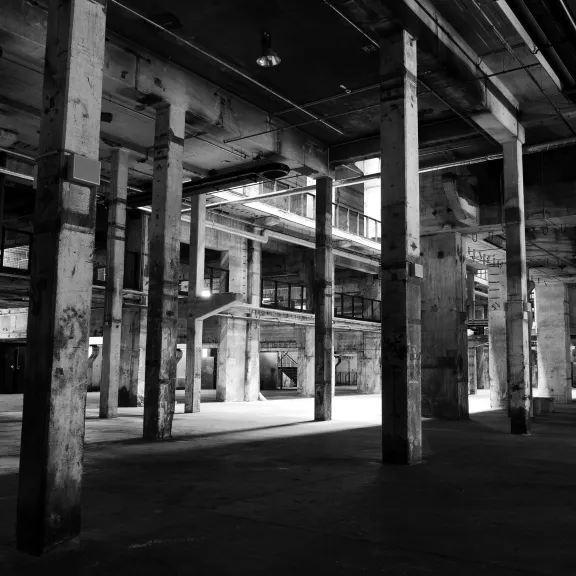 Schwarzweißfoto einer leeren, verlassenen Industriehalle mit vielen Säulen.