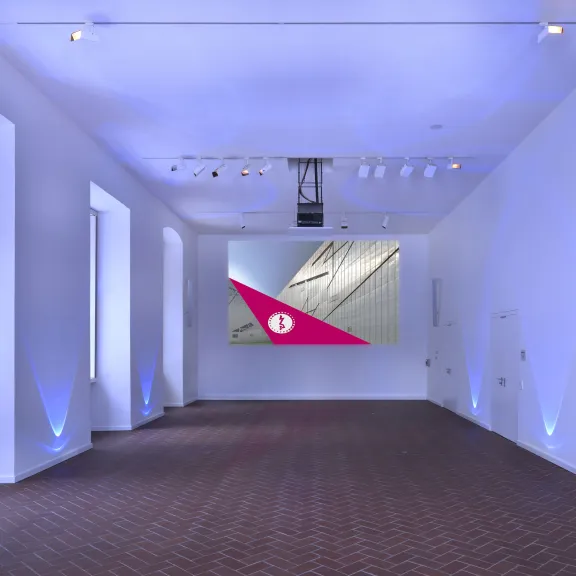 Moderner, leerer Ausstellungsraum mit blau beleuchteten Wänden und Leinwand vorne.