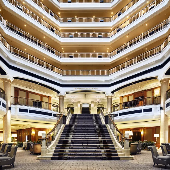 Großzügige Hotellobby mit breiter Treppe und mehreren Balkonetagen.