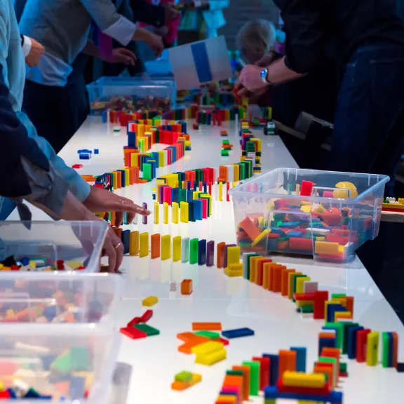 Meeting Guide Berlin Teamgeist Team baut eine Dominoreihe auf einem Tisch