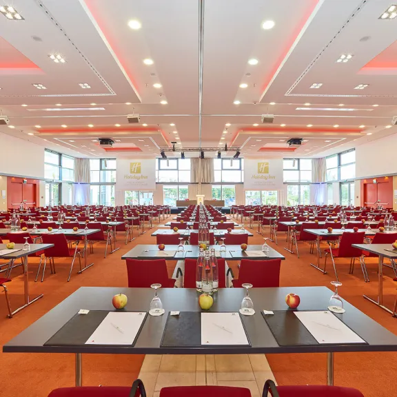 Großer, heller Konferenzsaal mit roten Stühlen und gedeckten Tischen.