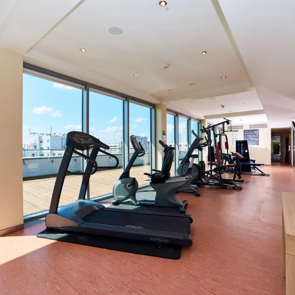 Heller Fitnessraum mit Laufbändern und großen Fenstern, Blick auf Terrasse.