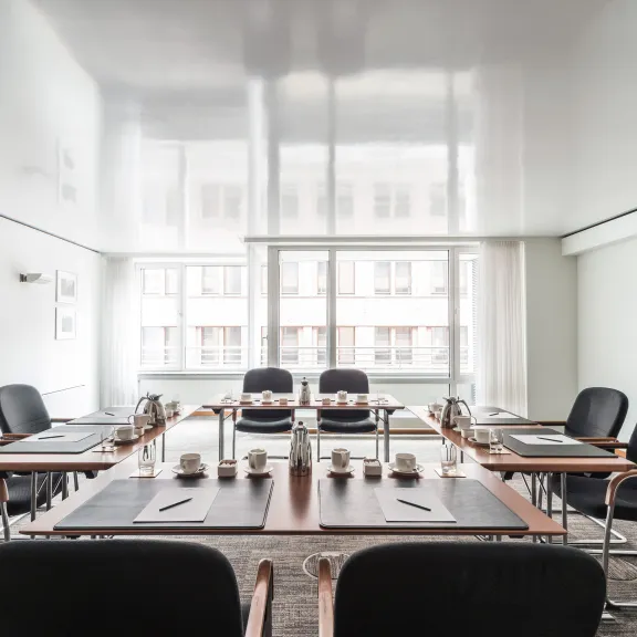 Moderner Konferenzraum mit großem Fenster, schwarzen Stühlen und gedecktem Tisch.