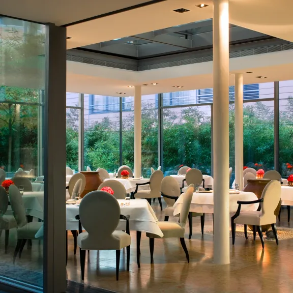 Modernes Restaurant mit weißen Tischen, stilvollen Stühlen und großen Fenstern.