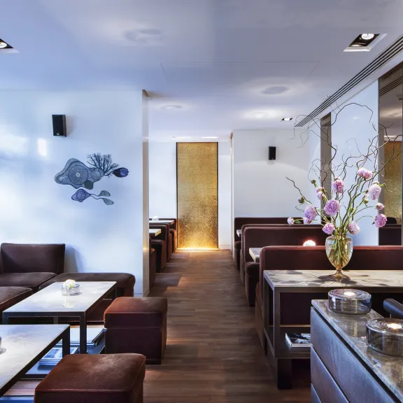 Modernes Café mit braunen Sofas, weißen Tischen und Blumenarrangement auf einer Kommode.