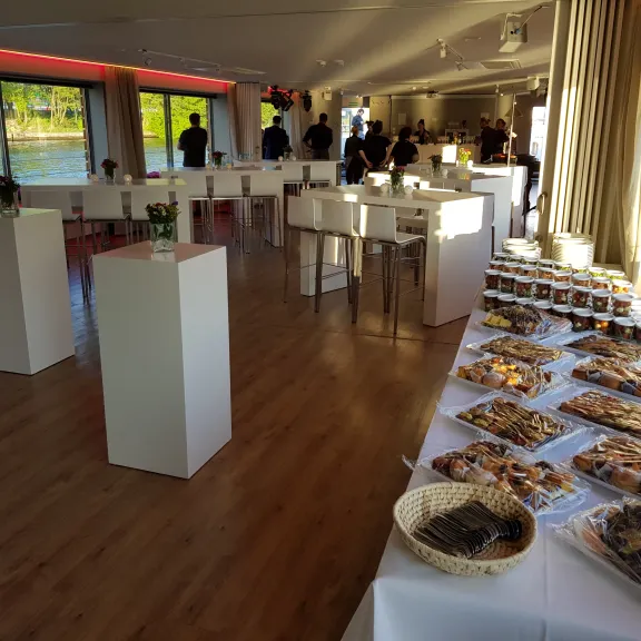 Buffet mit Gebäck in einem hellen Veranstaltungsraum, Menschen stehen im Hintergrund.