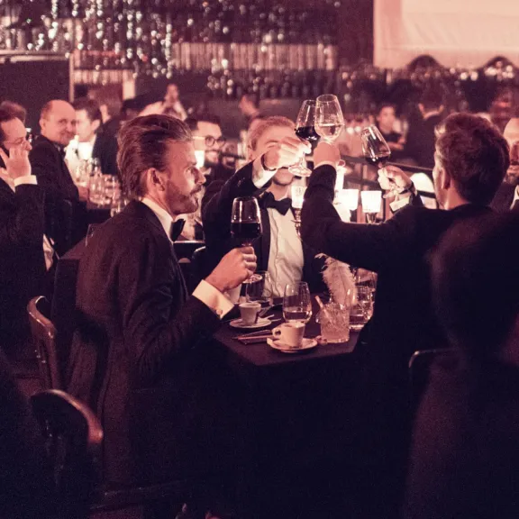 Männer im Anzug stoßen bei einem festlichen Abendessen mit Weingläsern an.