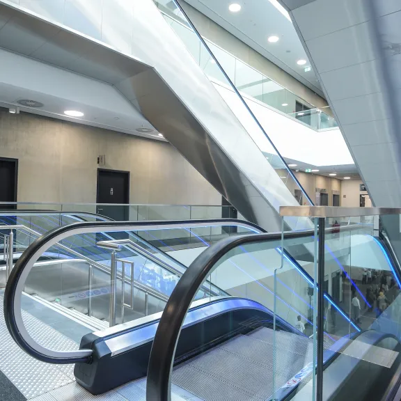 Moderne Rolltreppe in einem hellen, offenen Gebäude mit Betonwänden und Glasgeländern.