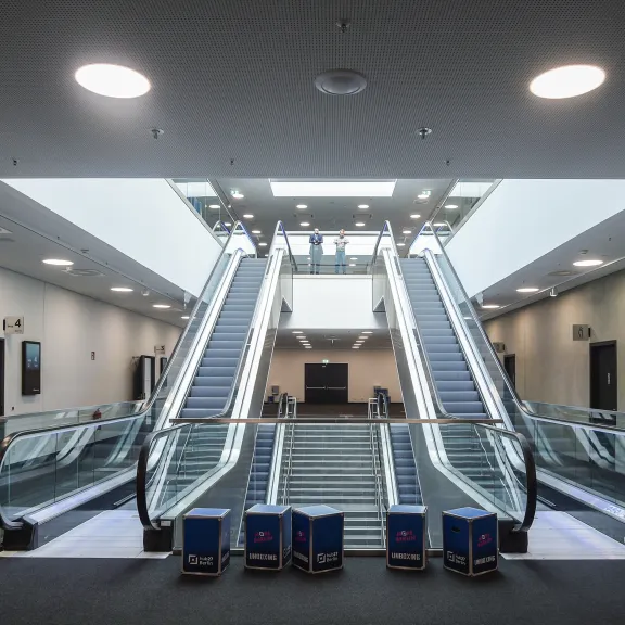 Breiter Flur mit drei Rolltreppen in modernem, hell beleuchtetem Gebäude.