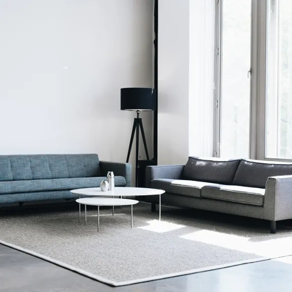 Helles Wohnzimmer mit zwei Sofas, Stehlampe und Couchtisch vor großem Fenster.