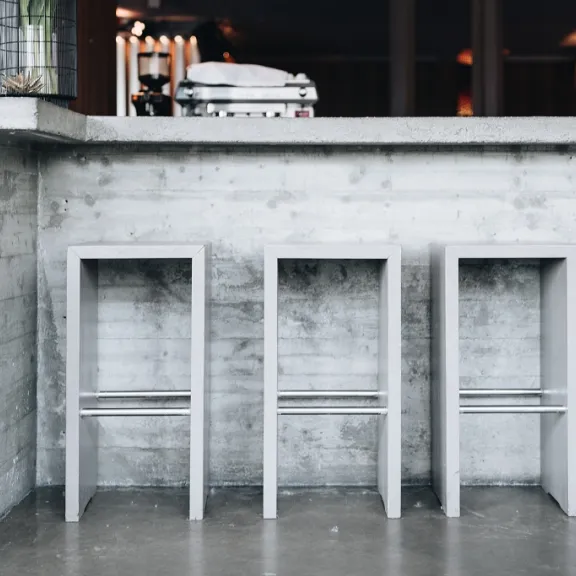 Drei graue Barhocker stehen vor einer Betonbar in modernem Café.