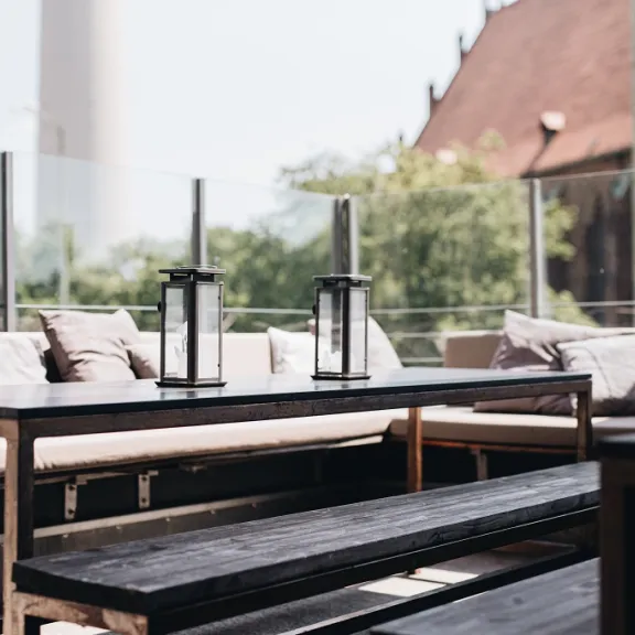 Moderne Terrasse mit Sofas, Kissen und Kerzenhaltern, im Hintergrund Glaswand und Gebäude.