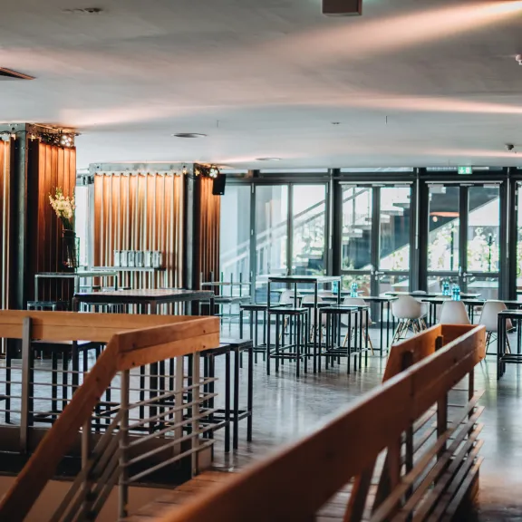 Modernes, lichtdurchflutetes Café mit Holzmöbeln und großen Fenstern.