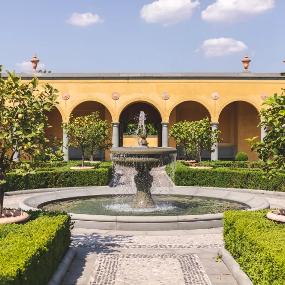 Springbrunnen im Garten mit Orangenbäumen und gelber Wand im Hintergrund