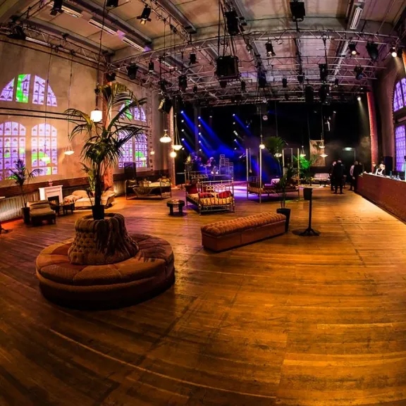 Großer, stimmungsvoll beleuchteter Veranstaltungsraum mit Sofas und bunten Lichtern.