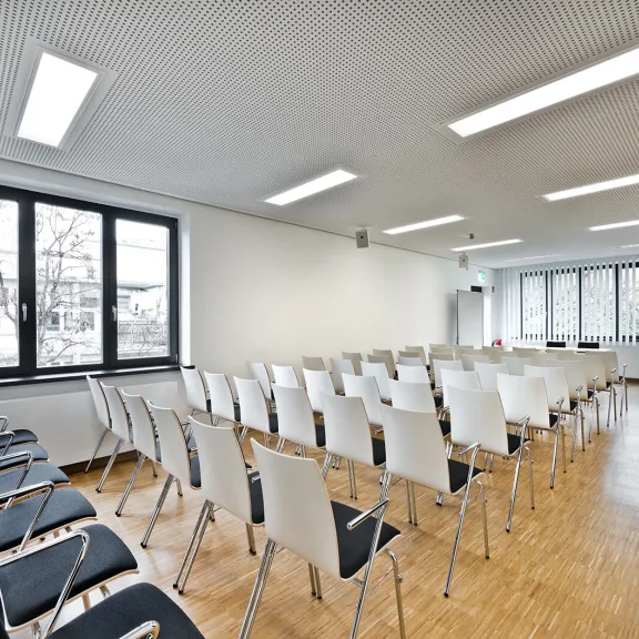 Heller, leerer Konferenzraum mit weißen Stühlen und großen Fenstern.