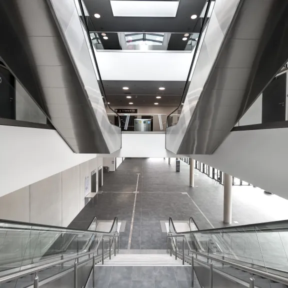 Breite Treppe mit Glasgeländer in modernem, hellen Gebäude mit Oberlicht.