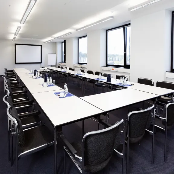 Heller Konferenzraum mit U-förmig gestellten Tischen und leeren Stühlen