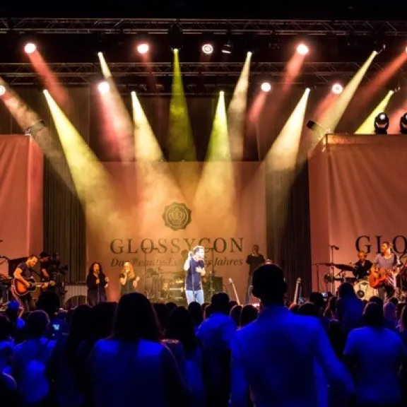 Konzertbühne mit Band, farbige Lichter und jubelndem Publikum.