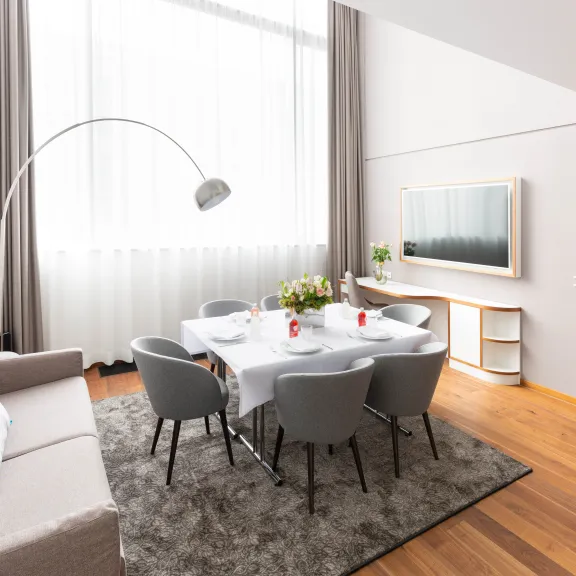 Modernes Esszimmer mit grauem Teppich, Esstisch, Sofa und großen Fenstern.