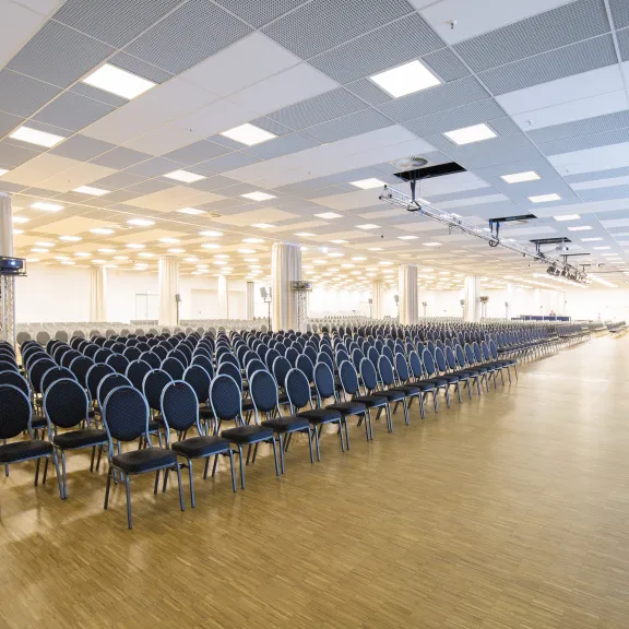 Großer leerer Konferenzsaal mit vielen Stuhlreihen und hellem Licht.