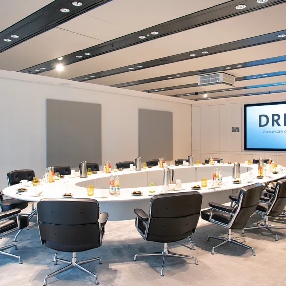 Moderner Konferenzraum mit rundem Tisch, schwarzen Stühlen und großem Bildschirm