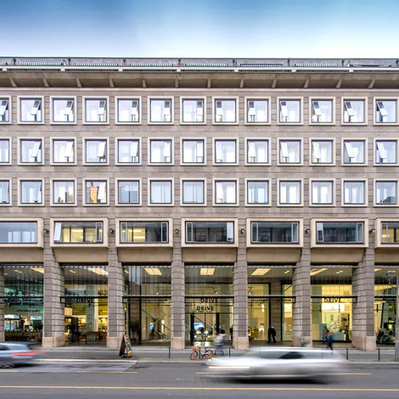 Modernes Bürogebäude mit Glasfassade und vorbeifahrenden Autos auf der Straße.
