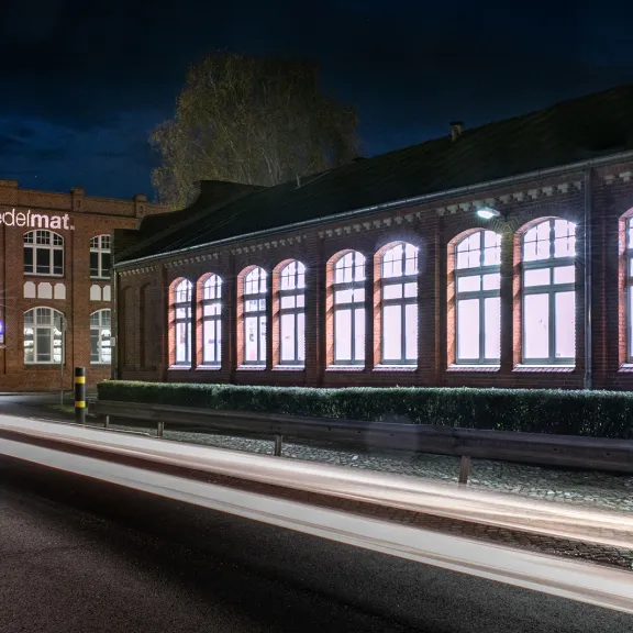 Beleuchtetes Backsteingebäude bei Nacht mit Lichtspuren auf der Straße.