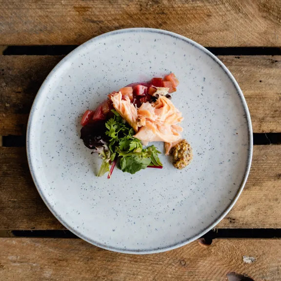Kleines Gericht mit Lachs, Salat und Dip auf weißem Teller, Holztisch als Untergrund.