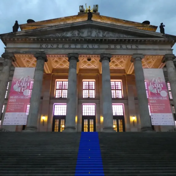 Großes klassisches Gebäude mit Säulen, beleuchtet, blauer Teppich auf der Treppe.