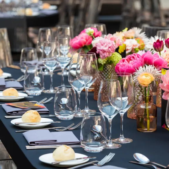 Festlich gedeckter Tisch mit Gläsern, Tellern und bunten Blumenarrangements.