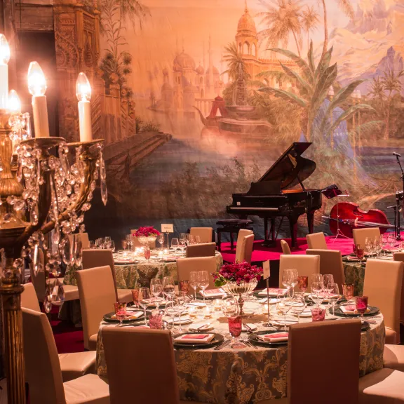 Festlich gedeckter Tisch vor Kronleuchter, Flügel im Hintergrund, warme Beleuchtung.