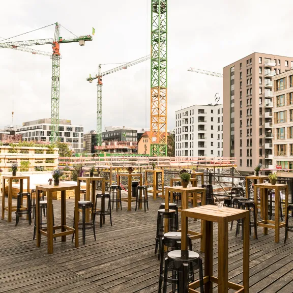 Dachterrasse mit Stehtischen, umgeben von Baustellen und modernen Gebäuden.