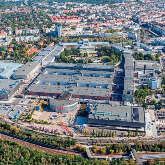 Luftaufnahme eines großen Messegeländes mit Hallen und umliegender Stadt.