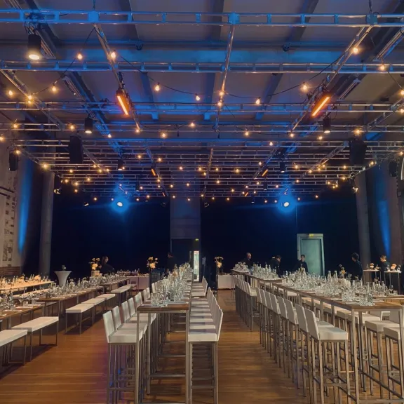 Festlich gedeckter Saal mit langen Tischen, dekoriert mit Lichterketten.