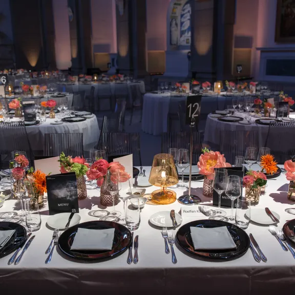 Elegant gedeckte Tische mit Blumen und Kerzen in festlich beleuchtetem Saal.