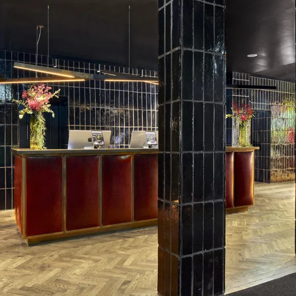 Moderne Hotelrezeption mit dunklen Fliesen und Blumenvasen auf dem Tresen.