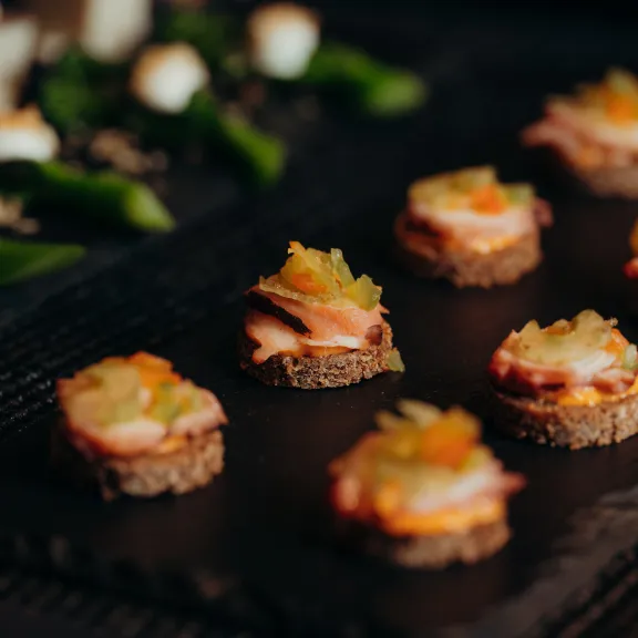 Kleine Canapés mit verschiedenem Belag auf einer schwarzen Servierplatte.