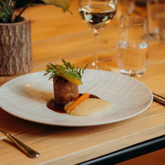 Elegantes Hauptgericht mit Fleisch, Soße, Gemüse und Püree auf gedecktem Holztisch.