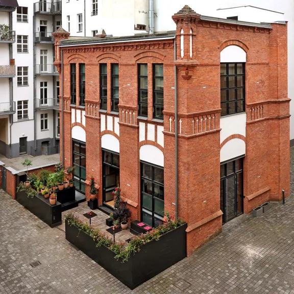 Backsteingebäude mit großen Fenstern und kleinem Innenhof mit Pflanzen und Sitzplätzen.