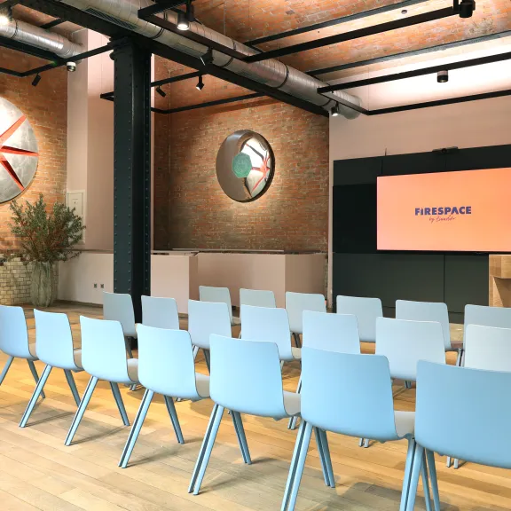 Moderner Seminarraum mit Stuhlreihen, Leinwand und Backsteinwänden.