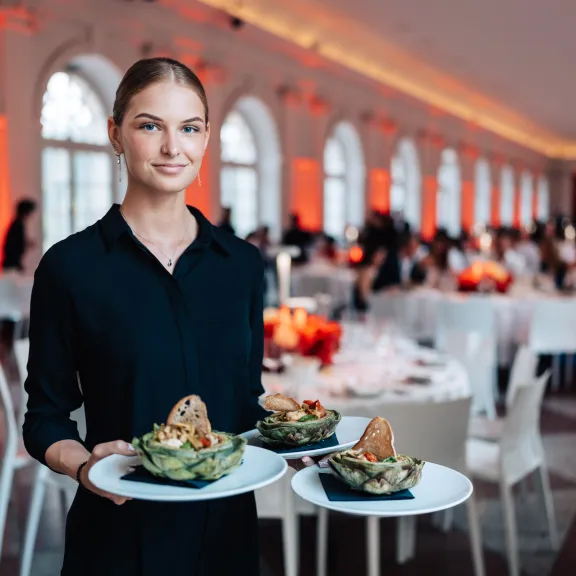 Kellnerin serviert Gerichte in elegantem, festlich beleuchtetem Saal.