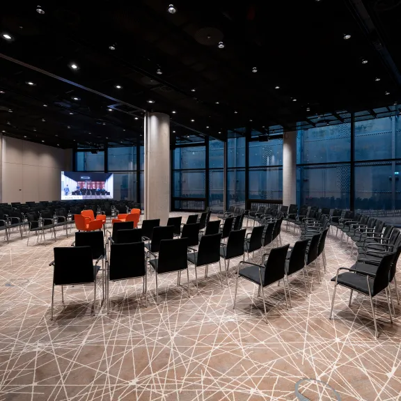 Moderner Konferenzraum mit schwarzen Stühlen im Halbkreis und zwei großen Bildschirmen.