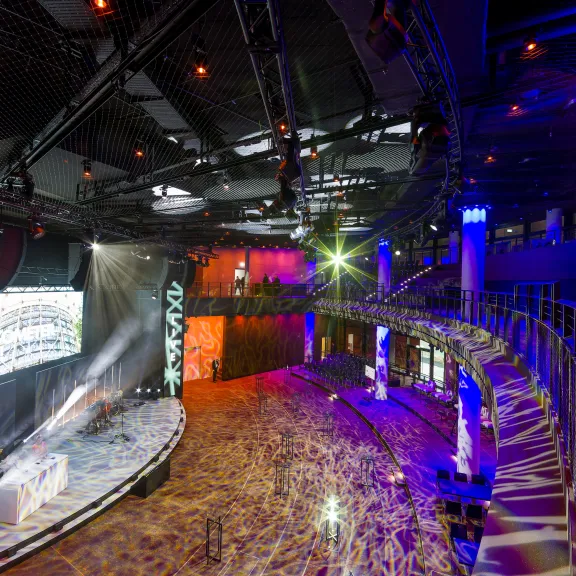 Bunte, moderne Veranstaltungshalle mit Bühne und leuchtenden Lichtern.