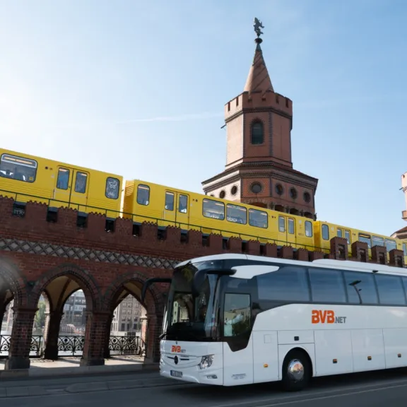Ein BVB.net Reisebusse fährt auf der Straße in Berlin, in Hintergrund eine U-Bahn.